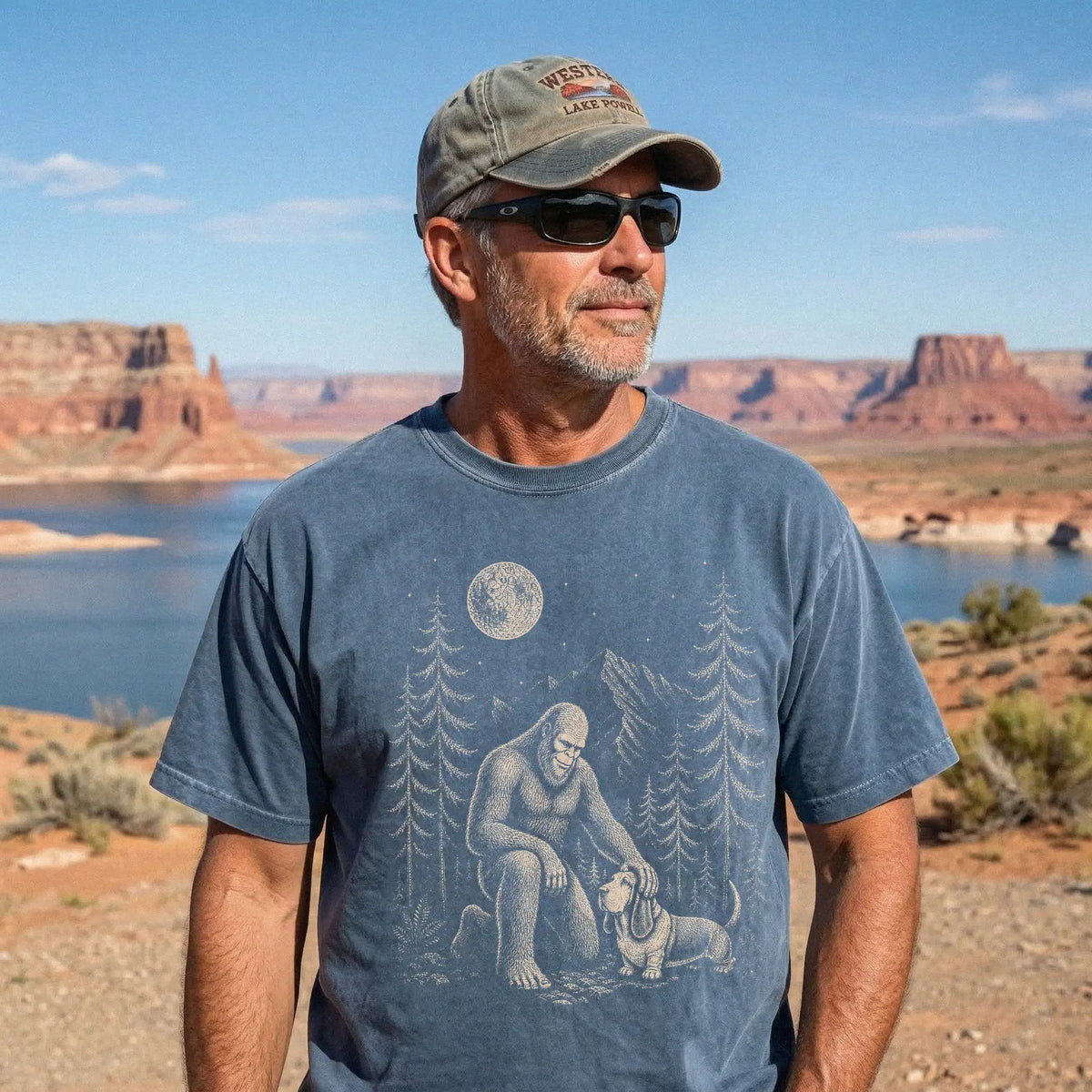 Model wearing a Denim Comfort Colors® T-shirt with bigfoot petting a basset hound beneath the moon in a pine forest