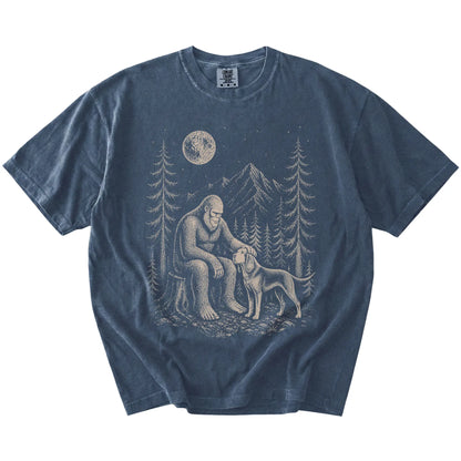Bigfoot petting a Bloodhound beneath the moon in a pine forest on a Denim Comfort Colors® T-shirt