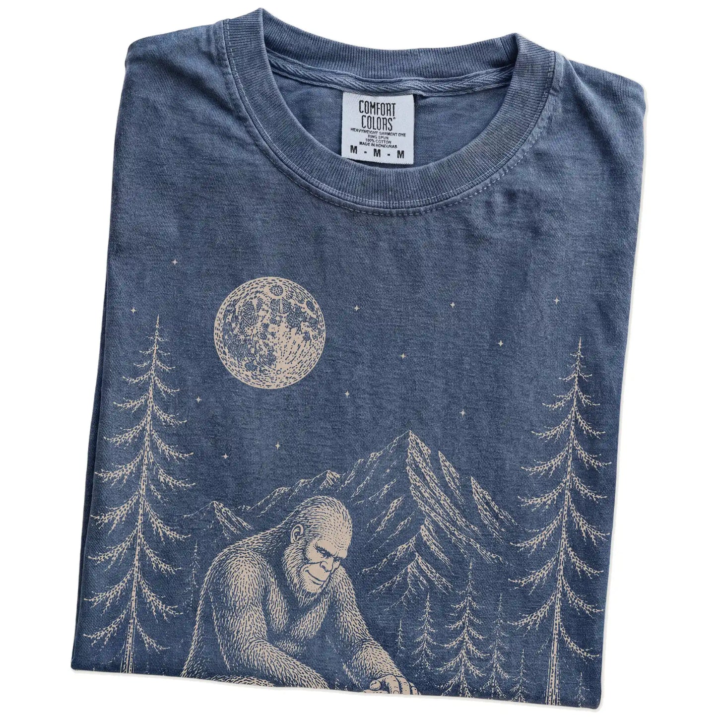 Folded Denim Comfort Colors® T-shirt showing bigfoot petting a bulldog beneath the moon in a pine forest