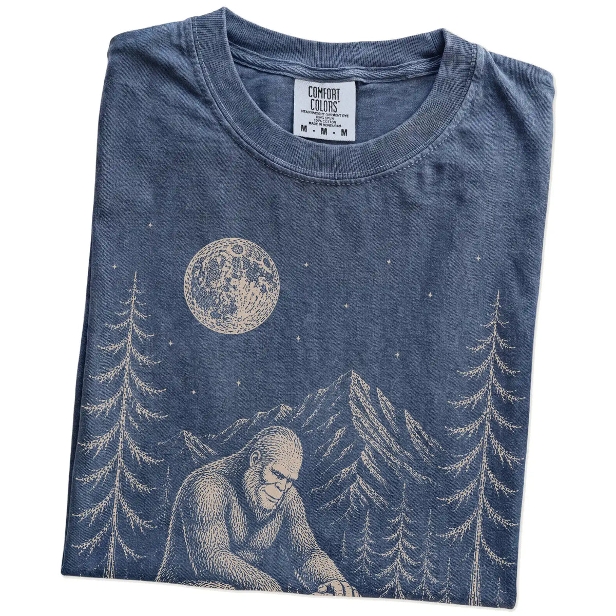 Folded Denim Comfort Colors® T-shirt showing bigfoot petting a bulldog beneath the moon in a pine forest