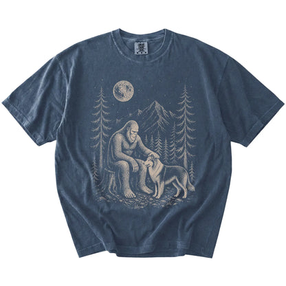 Bigfoot petting a Collie beneath the moon in a pine forest on a Denim Comfort Colors® T-shirt