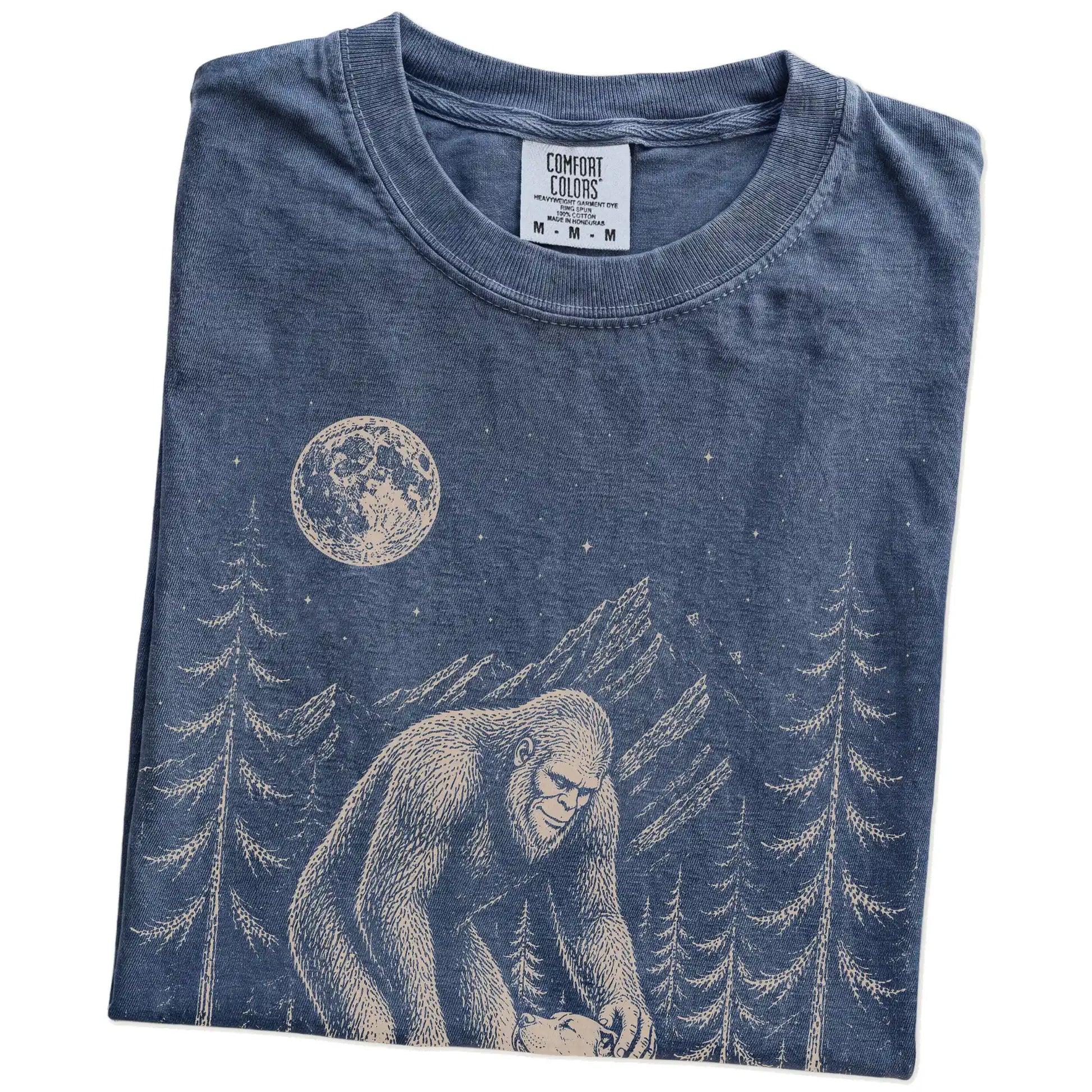 Folded Denim Comfort Colors® T-shirt showing bigfoot petting a pitbull beneath the moon in a pine forest