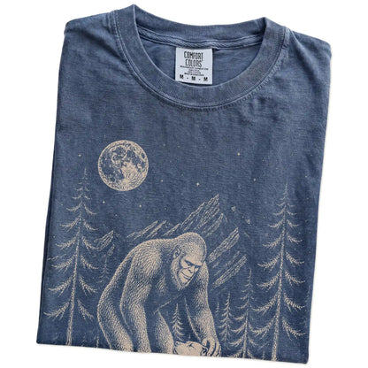 Folded Denim Comfort Colors® T-shirt showing bigfoot petting a pitbull beneath the moon in a pine forest