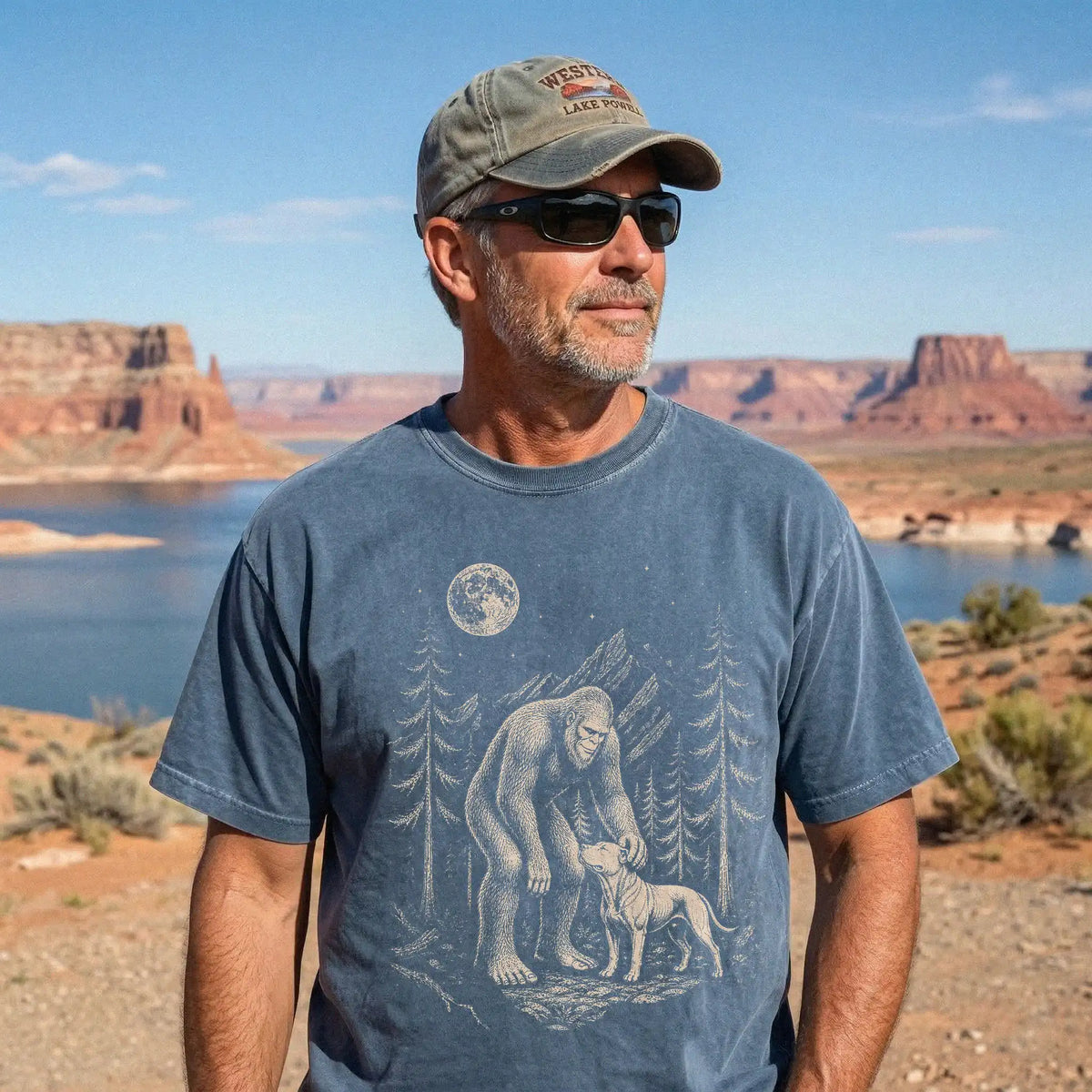 Model wearing a Denim Comfort Colors® T-shirt with bigfoot petting a pitbull beneath the moon in a pine forest