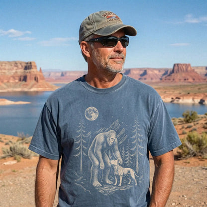 Model wearing a Denim Comfort Colors® T-shirt with bigfoot petting a pitbull beneath the moon in a pine forest