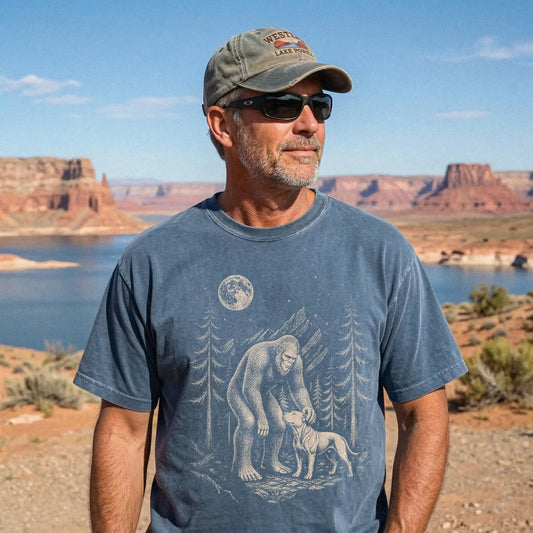 Model wearing a Denim Comfort Colors® T-shirt with bigfoot petting a pitbull beneath the moon in a pine forest