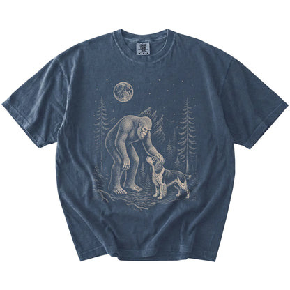 Bigfoot petting a Springer Spaniel beneath the moon in a pine forest on a Denim Comfort Colors® T-shirt