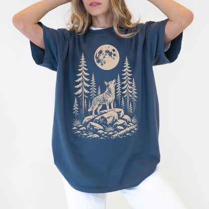 Model wearing a Denim Comfort Colors® T-shirt with a Blue Heeler howling beneath the moon and pine trees