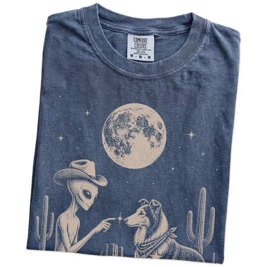 Folded Denim Comfort Colors® T-shirt showing cowboy alien fist-bumping a collie beneath the moon