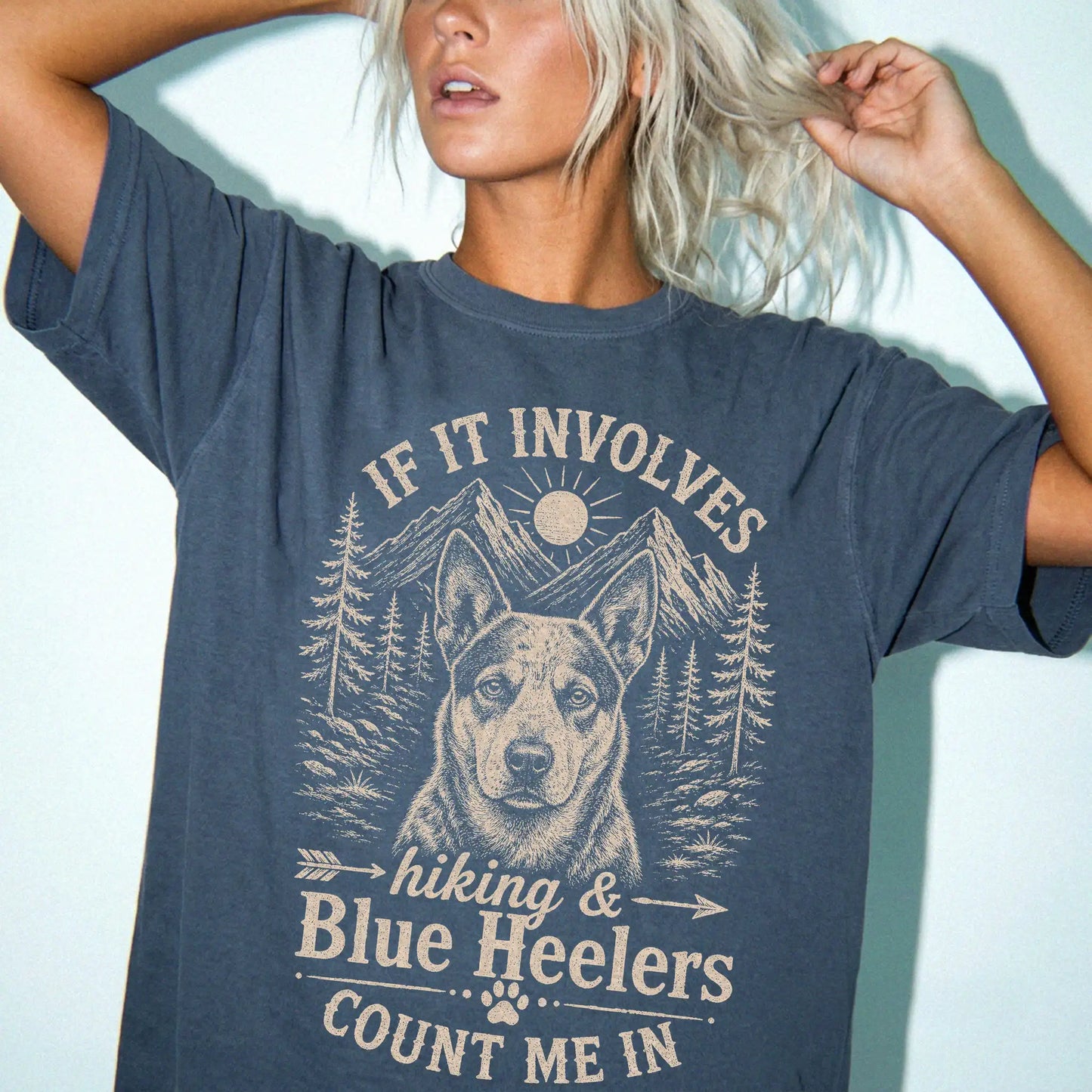 Model wearing a Denim Comfort Colors® T-shirt featuring Blue Heeler hiking design with mountain scenery