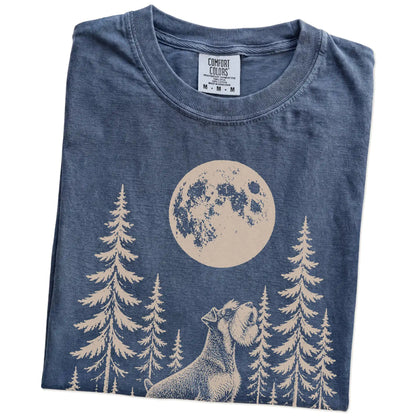 Folded Denim Comfort Colors® T-shirt showing a Standard Schnauzer howling beneath the moon and pine trees