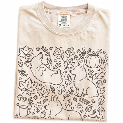 Folded Ivory Comfort Colors® T-shirt showing Corgi dogs with pumpkins, leaves, acorns, and woodland details