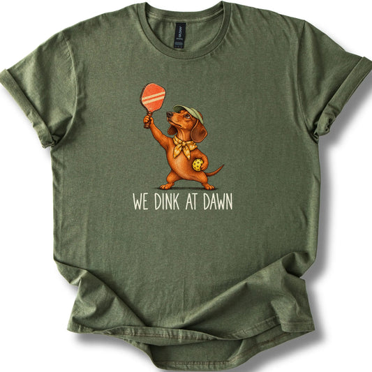Dachshund with a pickleball paddle and ball on a Military Green Gildan® T-shirt with We Dink at Dawn text