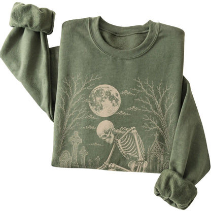 Folded Military Green sweatshirt with a skeleton petting a Bichon Frise in a graveyard
