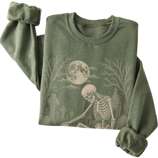 Folded Military Green sweatshirt with a skeleton petting a Cavalier in a graveyard