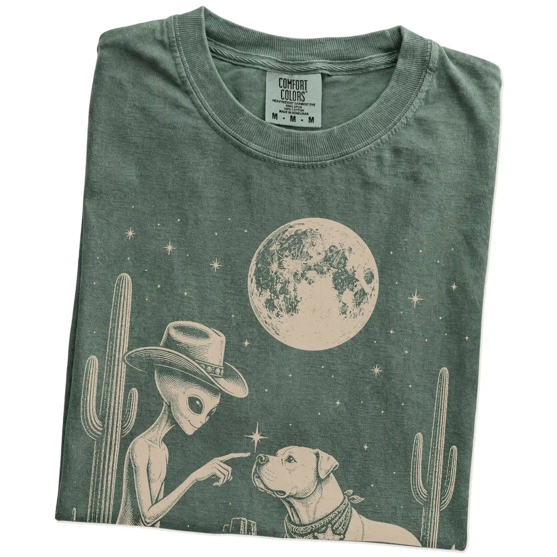 Folded Moss Comfort Colors® T-shirt showing cowboy alien fist-bumping a american bulldog beneath the moon