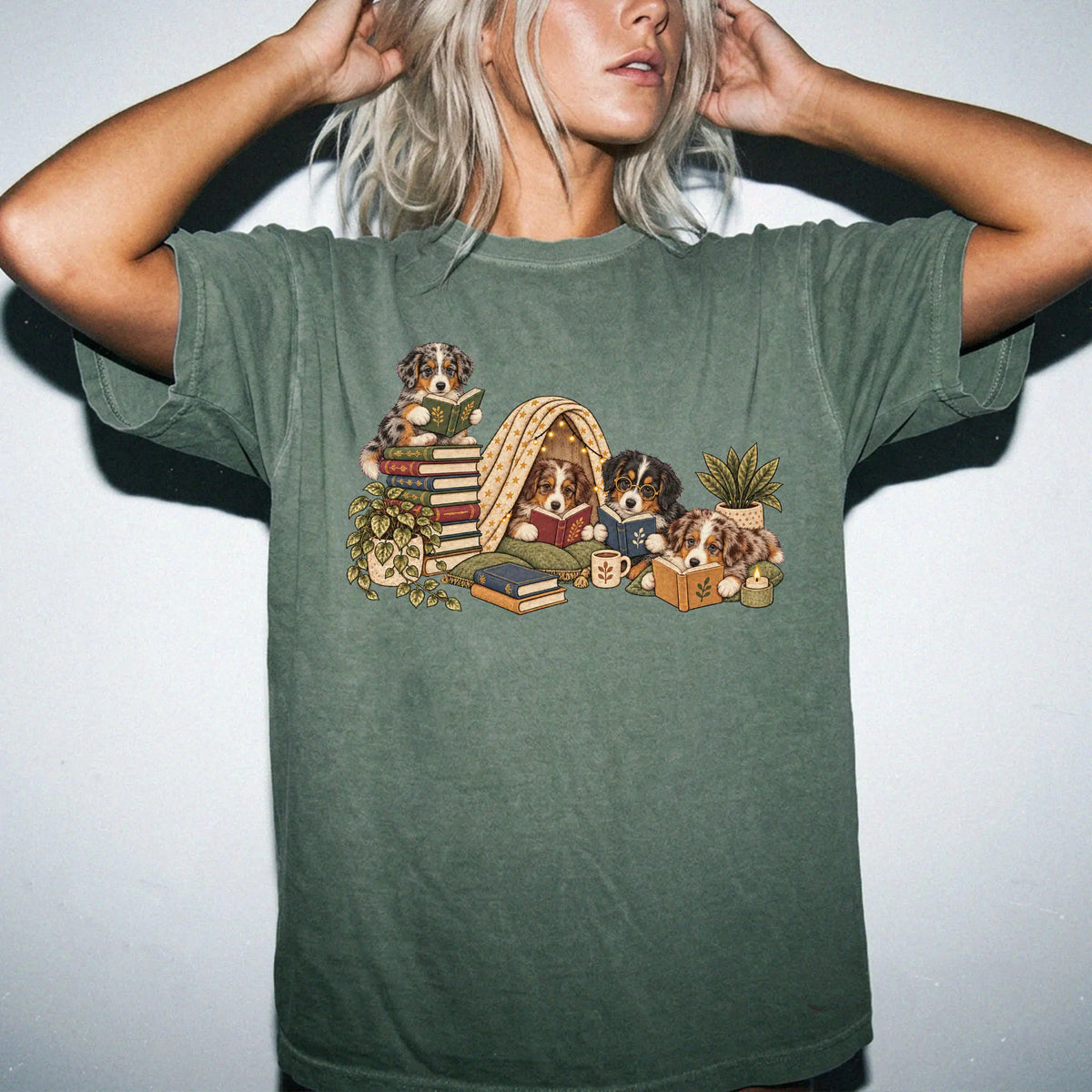 Australian Shepherd puppies reading books in a cozy blanket fort on a Moss T-shirt worn by a model