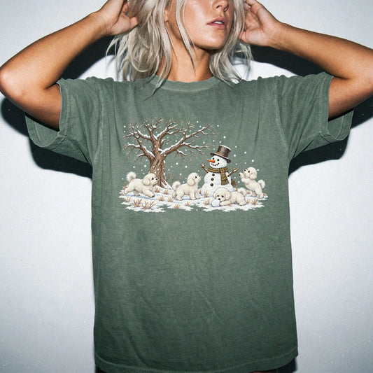 Bichon Frise puppies playing in snow with a snowman on a Moss T-shirt worn by a model