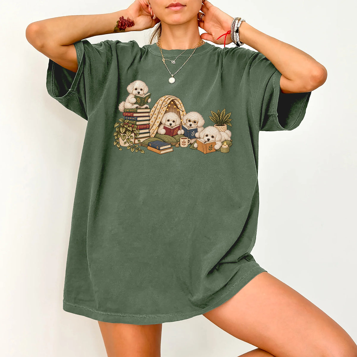 Bichon Frise puppies reading books in a cozy blanket fort on a Moss T-shirt worn by a model