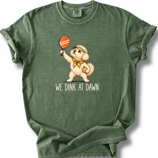 Bichon Frise with a pickleball paddle and ball on a Moss Comfort Colors® T-shirt with We Dink at Dawn text