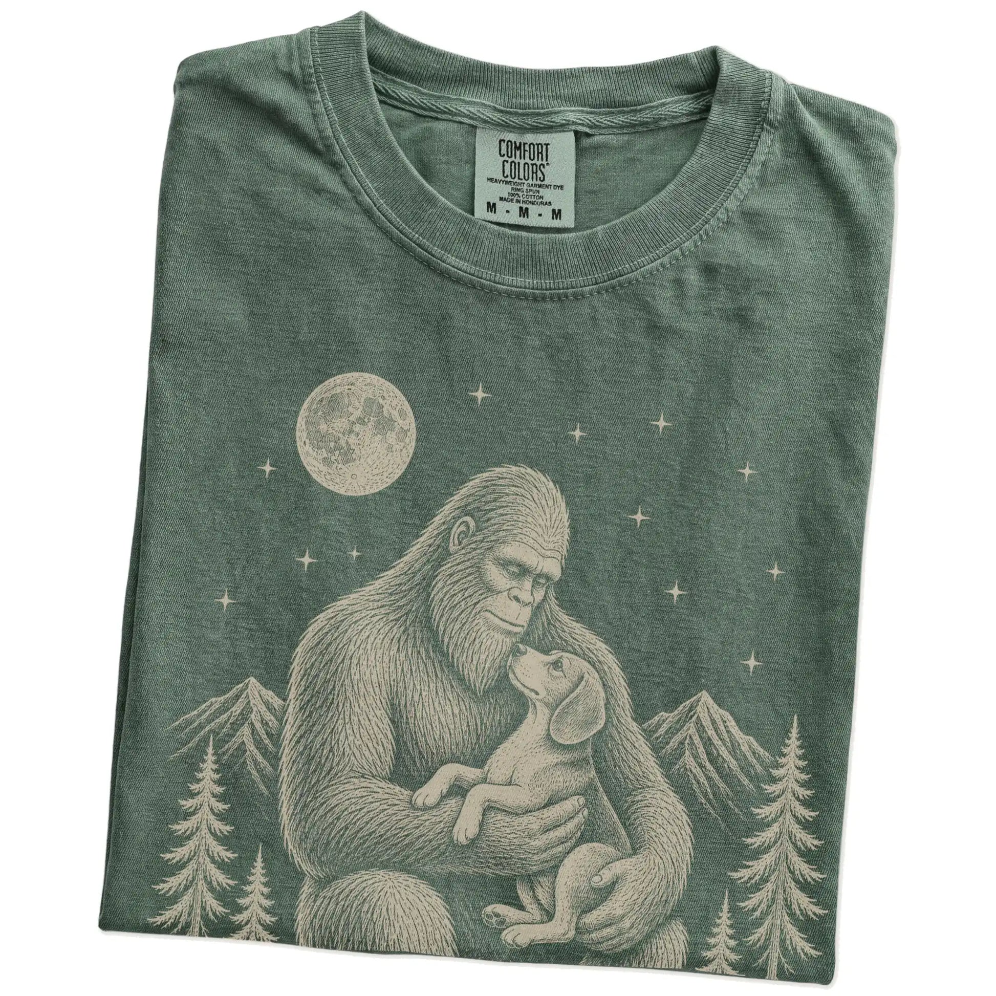 Folded Moss Comfort Colors® T-shirt showing Bigfoot holding a Beagle