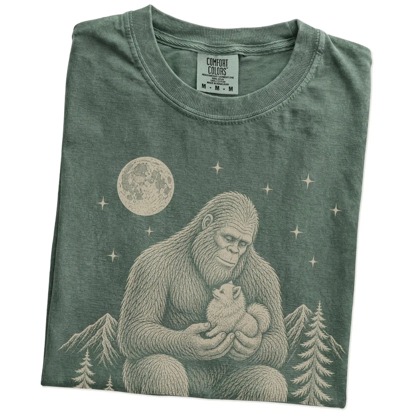 Folded Moss Comfort Colors® T-shirt showing Bigfoot holding a Pomeranian