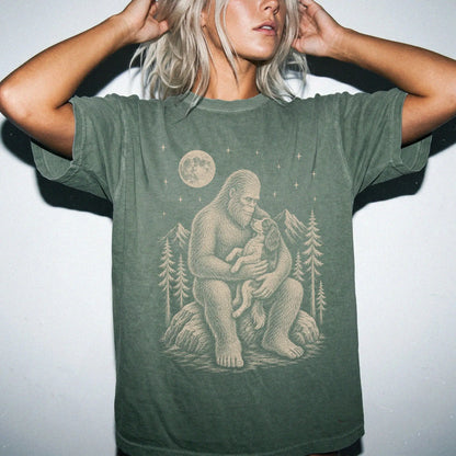 Model wearing a Moss Comfort Colors® T-shirt showing Bigfoot holding a Springer Spaniel