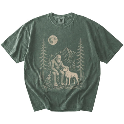 Bigfoot petting a American Bulldog beneath the moon in a pine forest on a Moss Comfort Colors® T-shirt