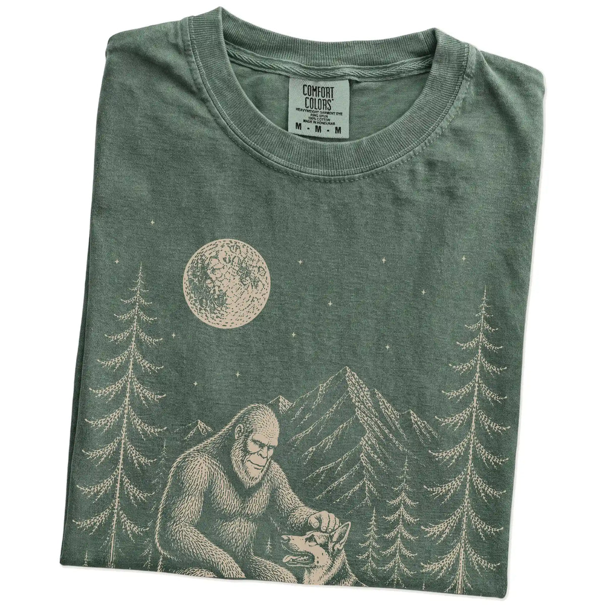 Folded Moss Comfort Colors® T-shirt showing bigfoot petting a german shepherd beneath the moon in a pine forest