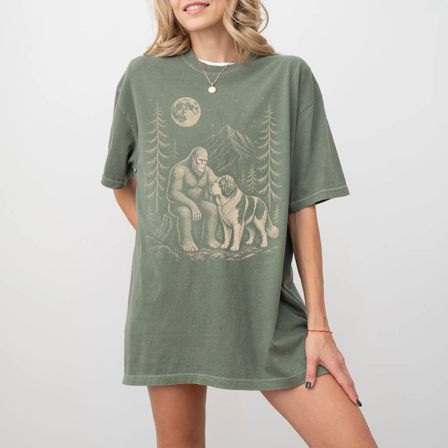 Model wearing a Moss Comfort Colors® T-shirt with bigfoot petting a saint bernard beneath the moon in a pine forest