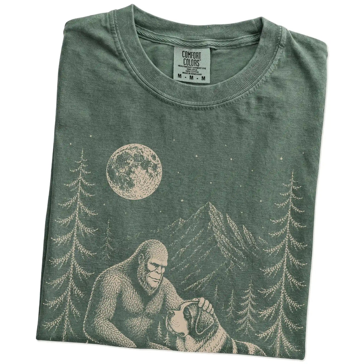 Folded Moss Comfort Colors® T-shirt showing bigfoot petting a saint bernard beneath the moon in a pine forest