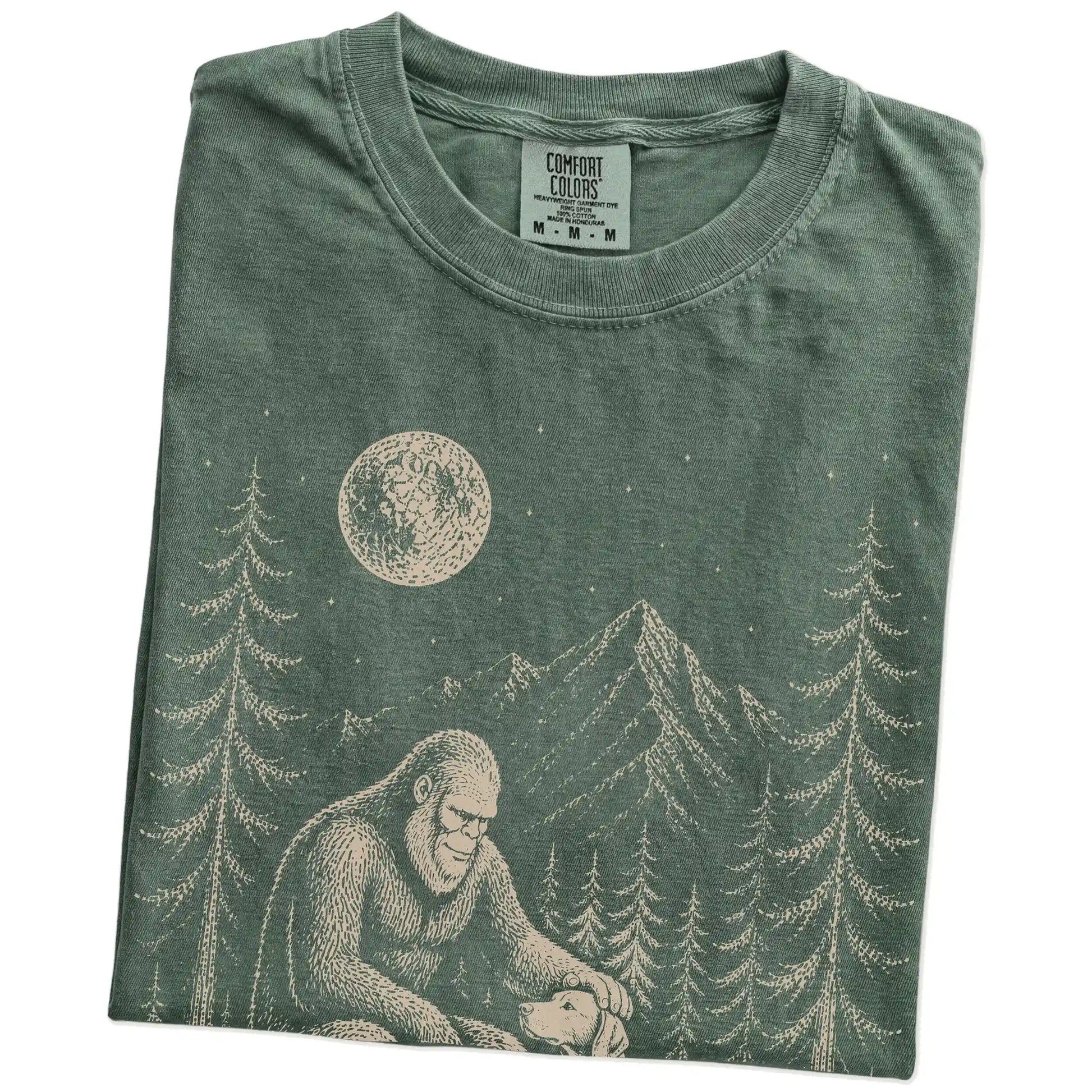 Folded Moss Comfort Colors® T-shirt showing bigfoot petting a vizsla beneath the moon in a pine forest