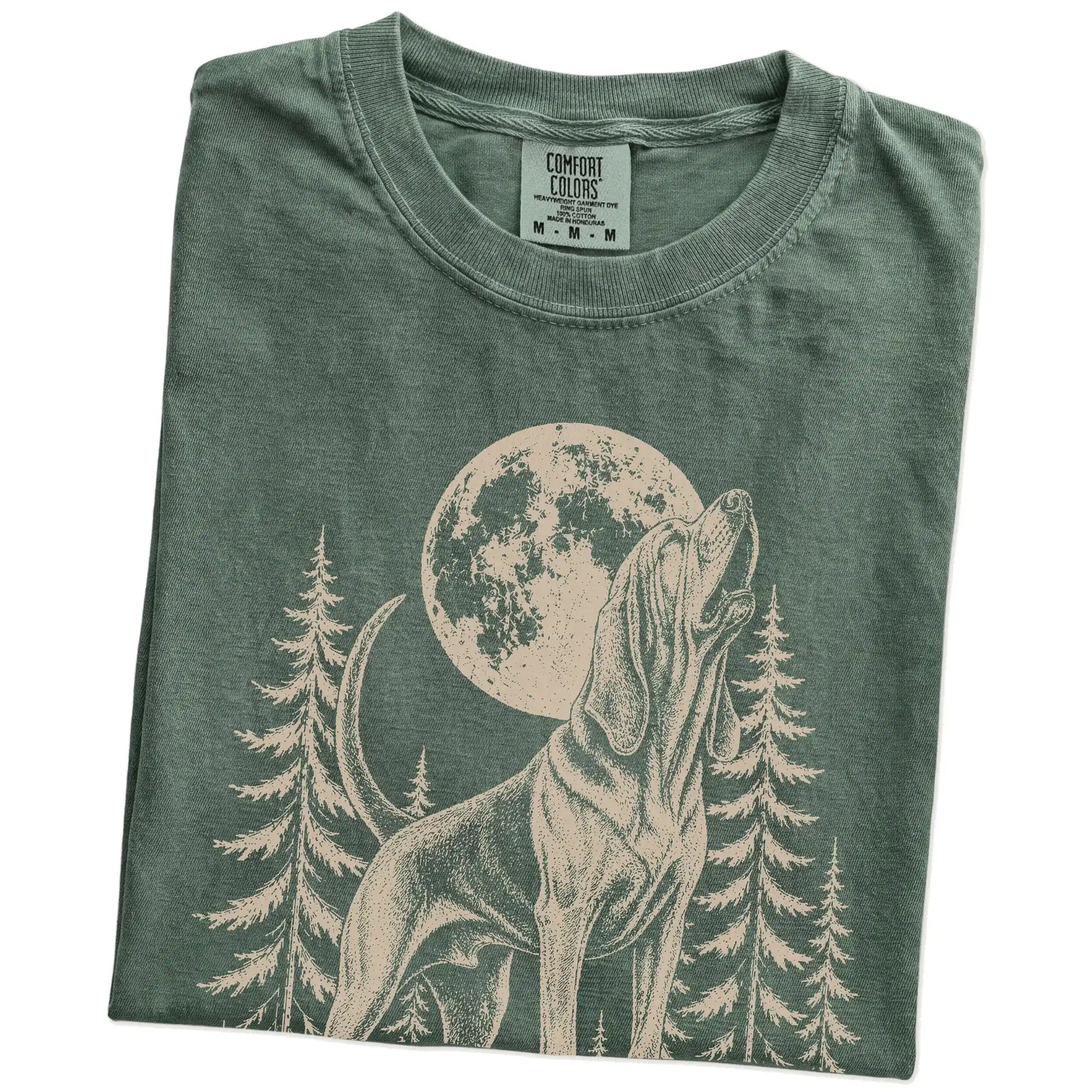 Folded Moss Comfort Colors® T-shirt showing a Bloodhound howling beneath the moon and pine trees