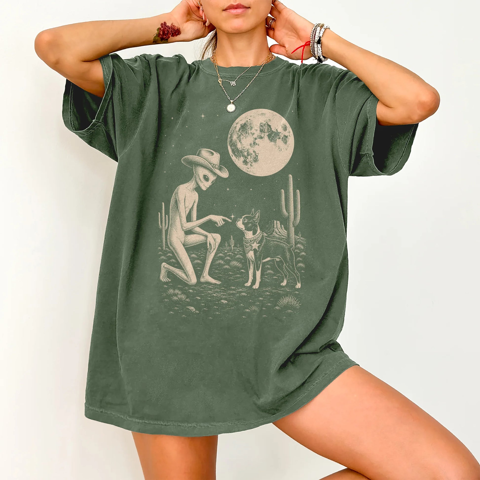 Model wearing a Moss Comfort Colors® T-shirt with cowboy alien fist-bumping a boston terrier beneath the moon