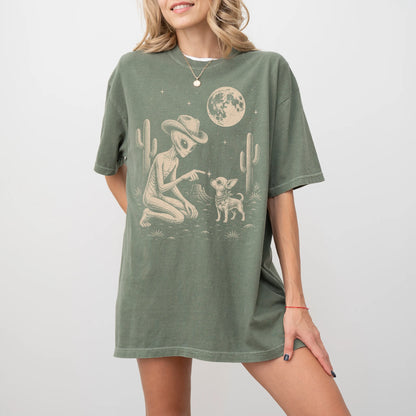 Model wearing a Moss Comfort Colors® T-shirt with cowboy alien fist-bumping a chihuahua beneath the moon