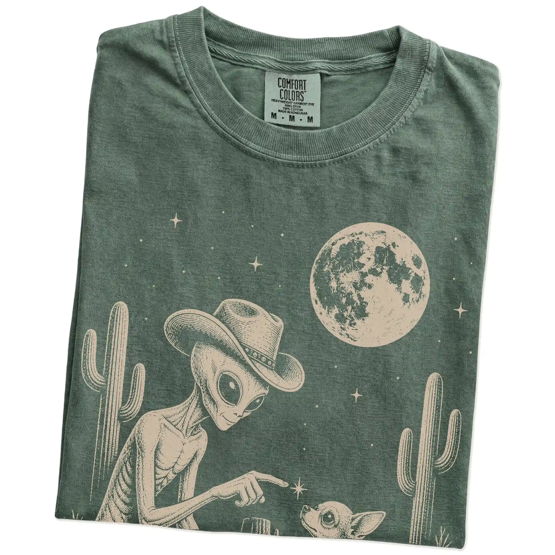 Folded Moss Comfort Colors® T-shirt showing cowboy alien fist-bumping a chihuahua beneath the moon