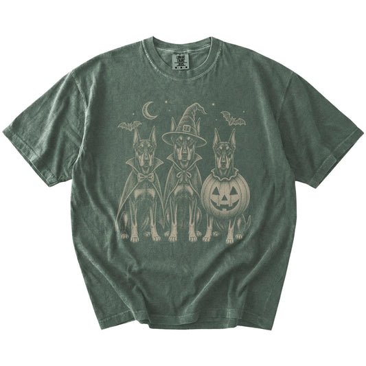 Three Doberman dogs dressed for Halloween beneath bats and a crescent moon on a Moss Comfort Colors® T-shirt
