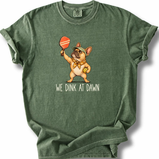 French Bulldog with a pickleball paddle and ball on a Moss Comfort Colors® T-shirt with We Dink at Dawn text