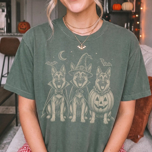 Model wearing a Moss Comfort Colors® T-shirt showing three German Shepherd dogs dressed for Halloween beneath bats and a cres
