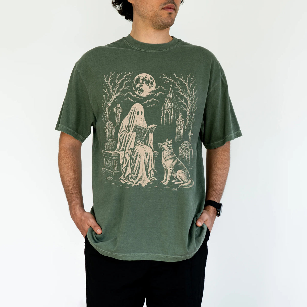 Model wearing a Moss Comfort Colors® T-shirt showing German Shepherd beside a reading ghost in a moonlit graveyard