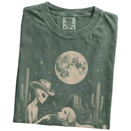 Folded Moss Comfort Colors® T-shirt showing cowboy alien fist-bumping a goldendoodle beneath the moon