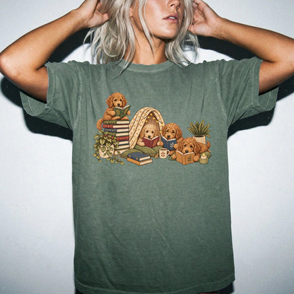 Goldendoodle puppies reading books in a cozy blanket fort on a Moss T-shirt worn by a model
