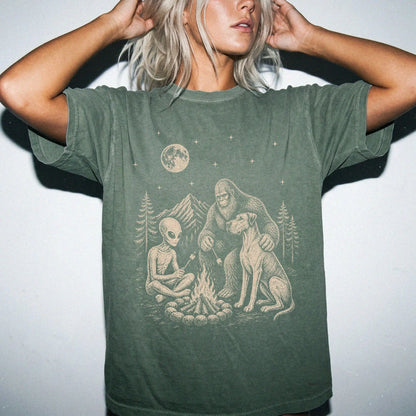 Model wearing a Moss Comfort Colors® T-shirt showing Great Dane camping with Bigfoot and an alien