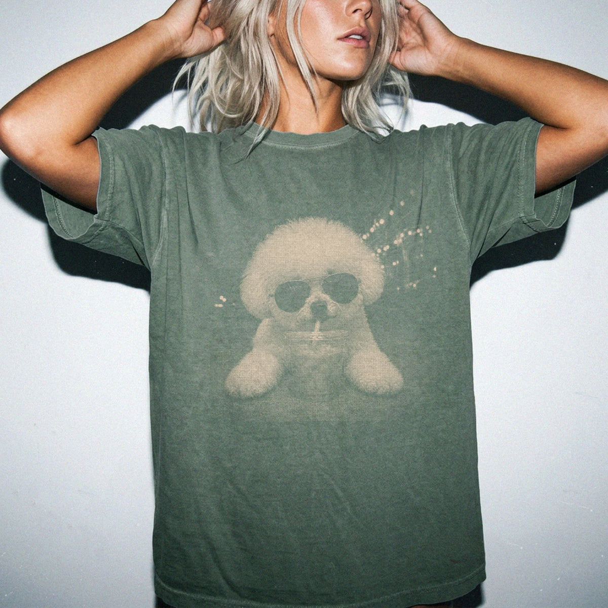 Model wearing a Moss Comfort Colors® T-shirt featuring Bichon Frise with iced coffee in a retro grunge design