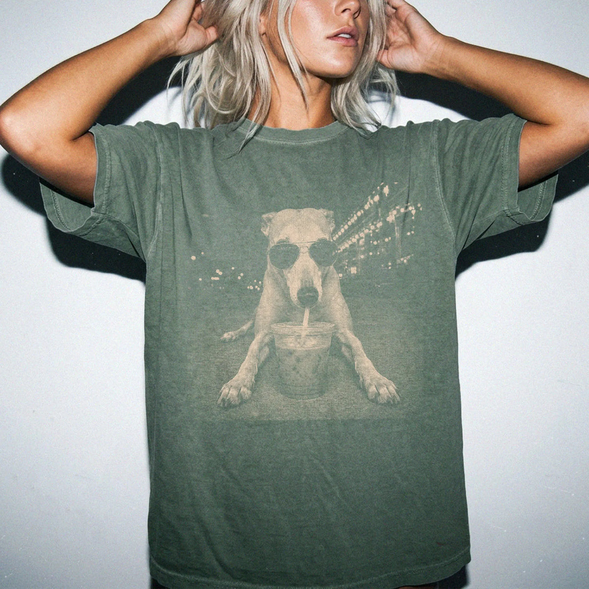 Model wearing a Moss Comfort Colors® T-shirt featuring Greyhound with iced coffee in a retro grunge design
