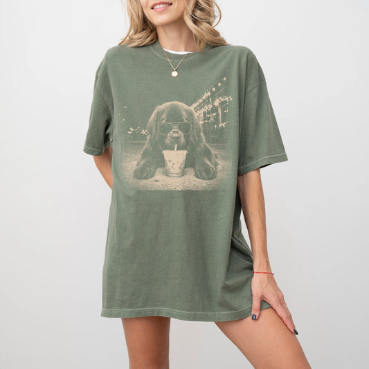 Model wearing a Moss Comfort Colors® T-shirt featuring Newfie with iced coffee in a retro grunge design