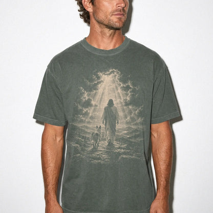 Person wearing a Moss T-shirt with Jesus walking beside a Blue Heeler beneath rays of light