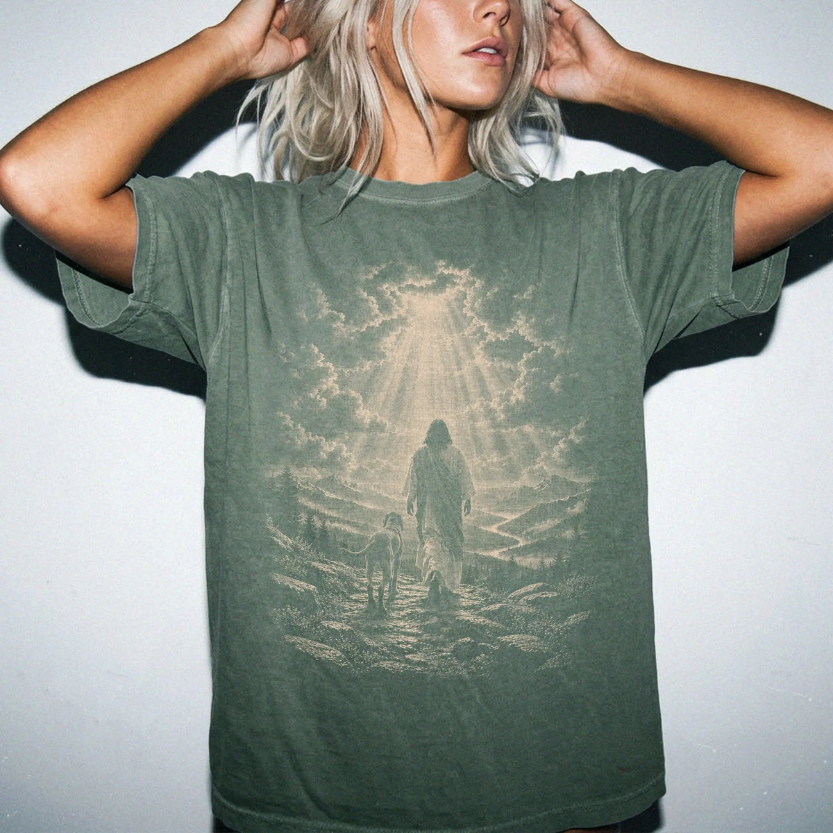 Person wearing a Moss T-shirt with Jesus walking beside a Weimaraner beneath rays of light