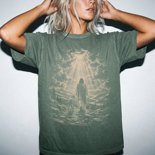 Person wearing a Moss T-shirt with Jesus walking beside a Weimaraner beneath rays of light