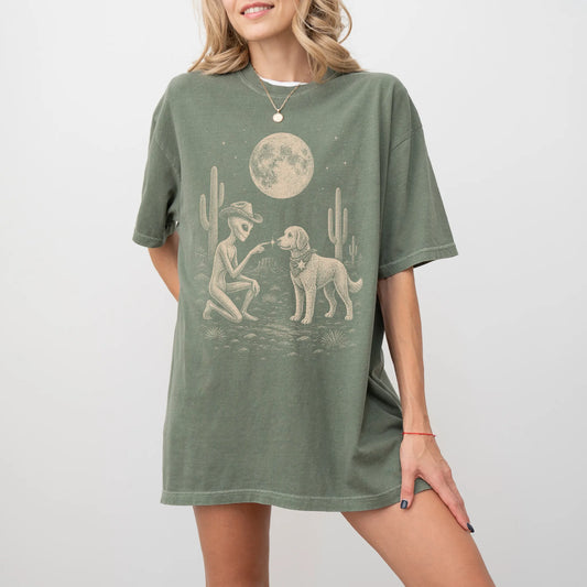 Model wearing a Moss Comfort Colors® T-shirt with cowboy alien fist-bumping a labradoodle beneath the moon